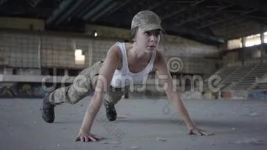 穿着军装的年轻女子从一栋废弃建筑的混凝土地板上扭动身体。 女人训练